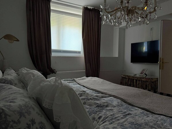 A bedroom with a bed, a television, a chandelier, and a window with curtains.