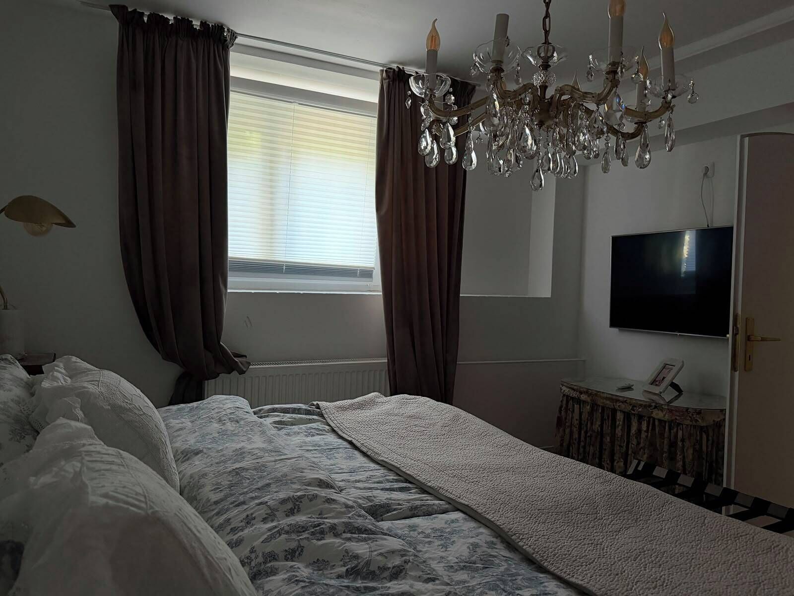 Ein Schlafzimmer mit einem Bett, einer Kandelaber, einem Fernseher und einem Fenster mit Vorhängen.