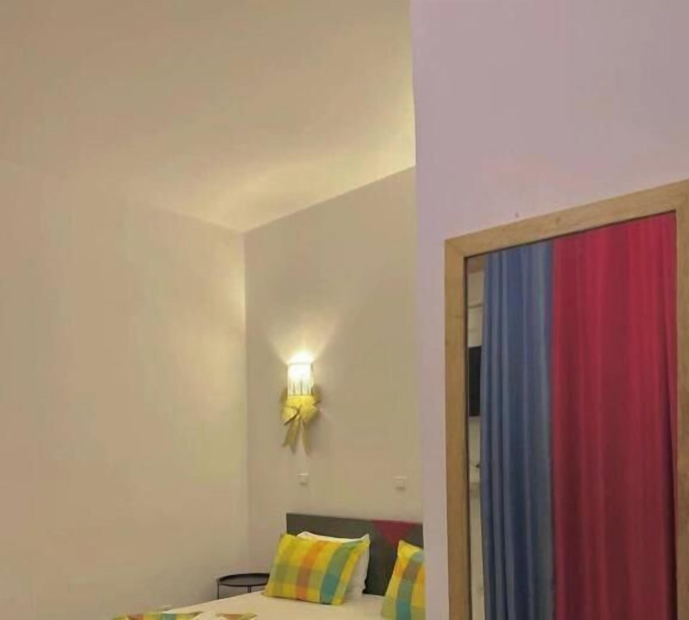 Een slaapkamer met een bed, een wandlamp en een deur met gordijn.
