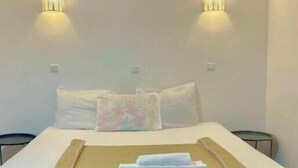 Habitación de hotel con cama, dos luces de pared, una mesita de noche y una toalla doblada sobre la cama.