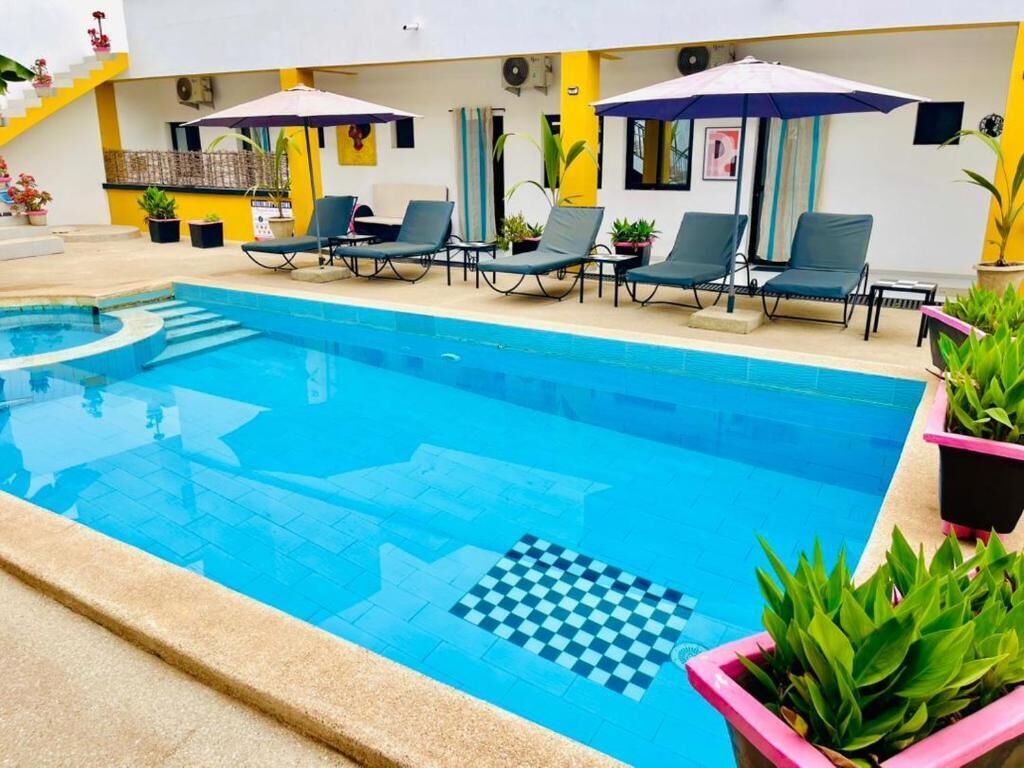 A swimming pool with lounge chairs and umbrellas, surrounded by potted plants.