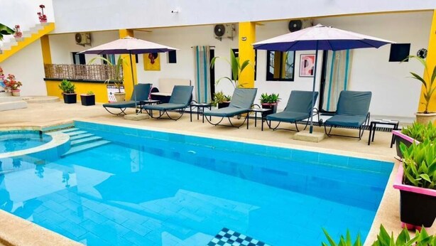 Una piscina con sillas de descanso y sombrillas, rodeada de plantas en macetas.