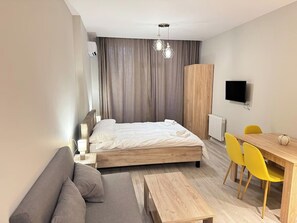 A modern bedroom with a bed, a sofa, a dining table with chairs, a TV, and a wardrobe. - Cozy 1-bedroom studio in peaceful Batumi with AC (Batumi)