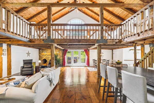 A spacious room with a high ceiling, wooden beams, a fireplace, and a dining area with chairs and a table.