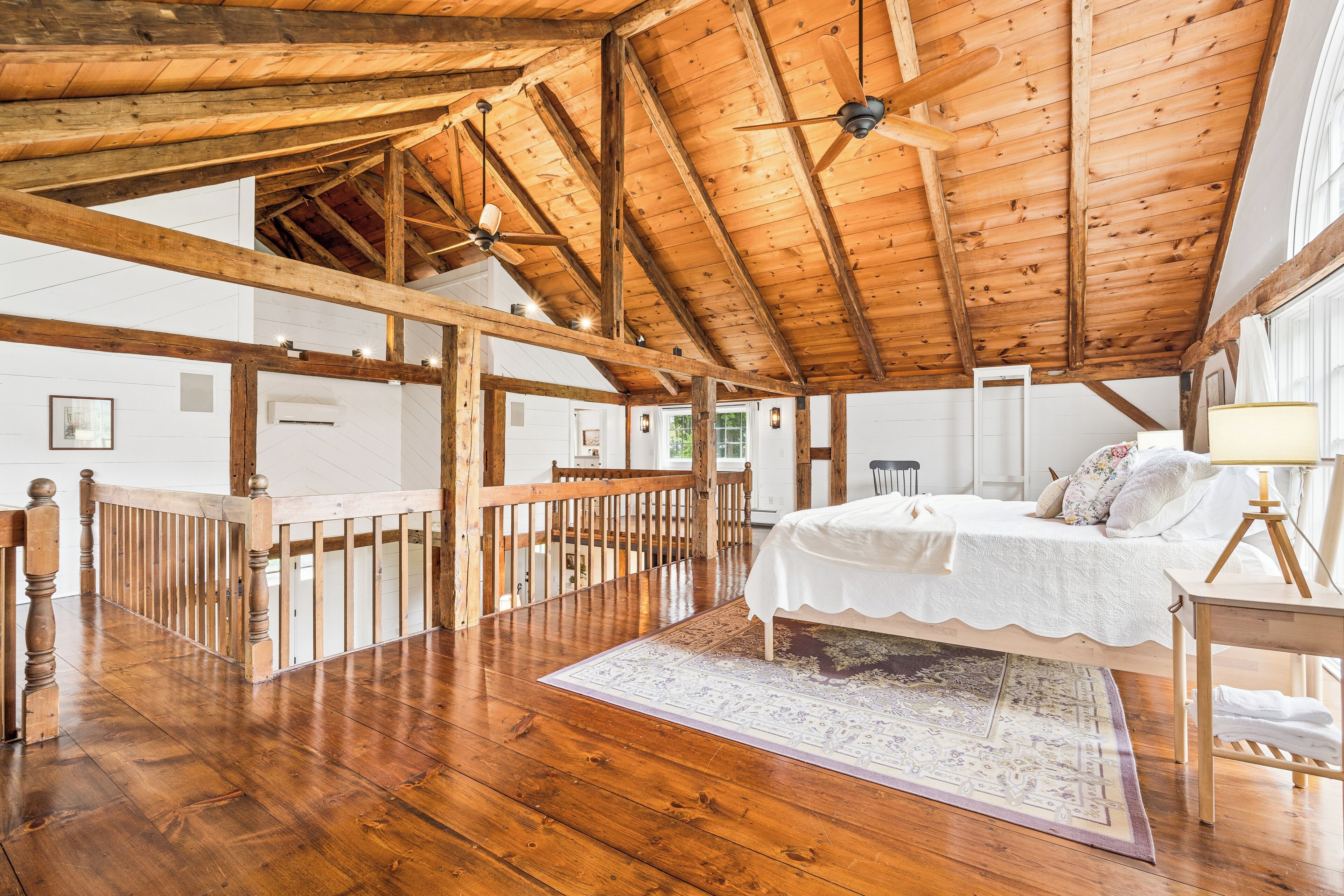 Un dormitorio amplio con techo de madera, una cama grande, una mesita de noche y vistas al exterior.