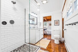 Un baño moderno con cabina de ducha de vidrio, inodoro blanco y suelo de madera.