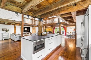 A spacious kitchen with a central island, wooden beams, and a stone fireplace.