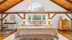 Ein Schlafzimmer mit einem großen Bett, Holzbalken, einem Fenster und einem Schreibtisch mit Stuhl.
