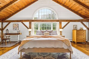 Un dormitorio con una cama grande, vigas de madera, un ventanal y un escritorio con una silla.