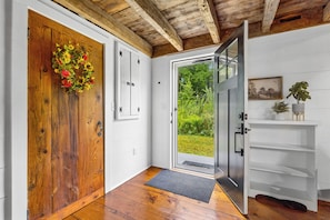 A wooden door with a flower wreath, a white wall with a picture, and a glass door leading to a garden.