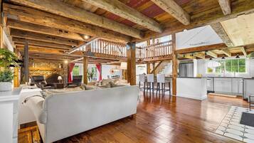 Un vaste espace de vie doté d’un plafond en bois, d’un canapé, d’un coin cuisine avec un bar et d’un mur en pierre.