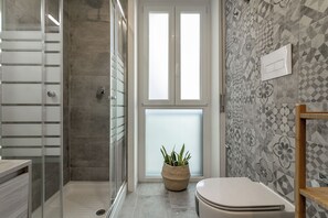 Ein Badezimmer mit Duschkabine aus Glas, Toilette, Waschbecken und einer Topfpflanze.