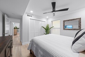 A bedroom with a bed, a ceiling fan, a window with blinds, a mirror, and a door leading to a hallway. - Kings Crown #114 | Beach View Luxury & Sanibel Island Charm (Sanibel)
