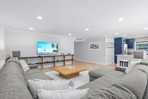 Ein modernes Wohnzimmer mit einem großen Flachbildfernseher, einem Holztisch und grauen Sofas.