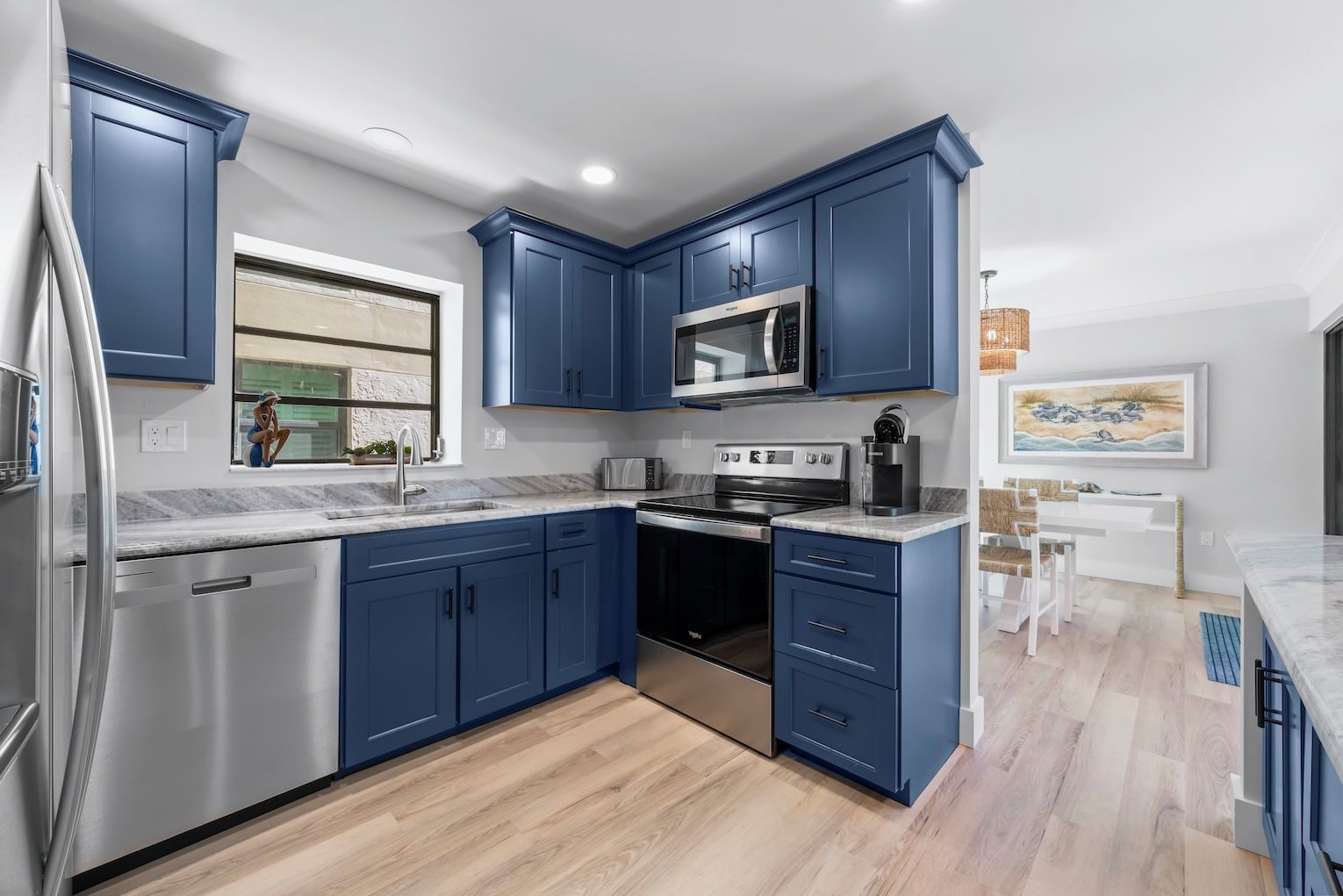 A modern kitchen with blue cabinets, stainless steel appliances, and a wooden floor.