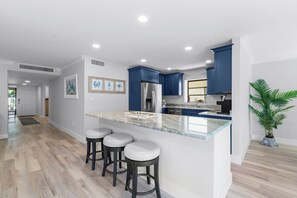 A modern kitchen with a marble countertop, blue cabinets, and a central island with bar stools. - Kings Crown #114 | Beach View Luxury & Sanibel Island Charm (Sanibel)