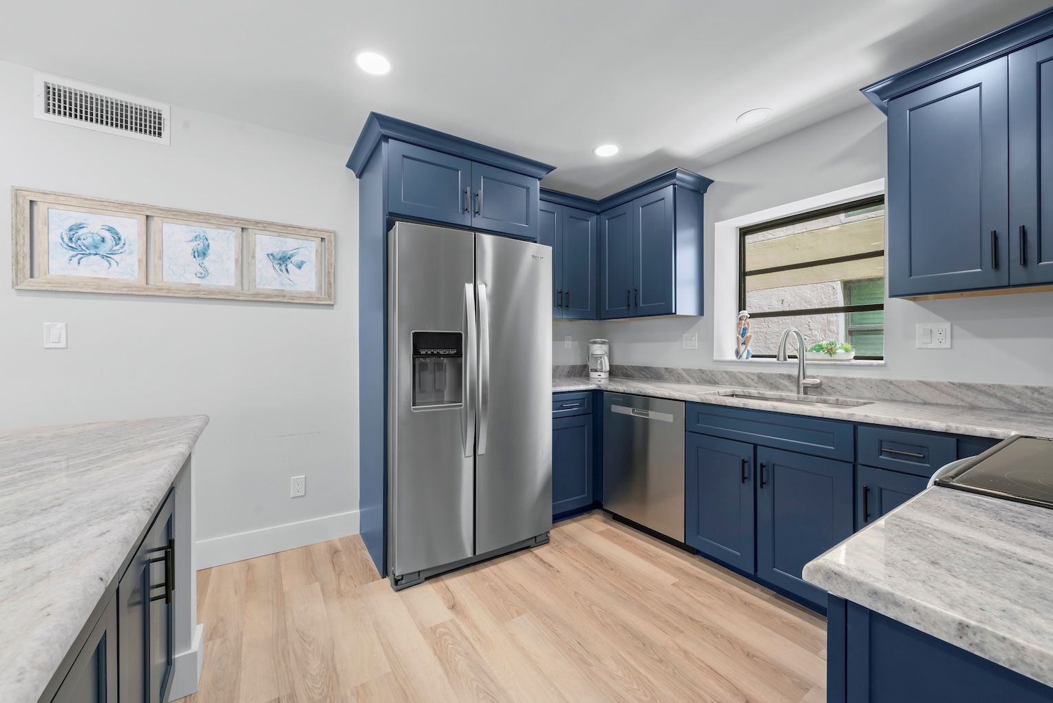 A modern kitchen with blue cabinets, stainless steel appliances, and a marble countertop.