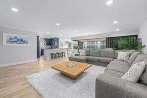 A modern living room with a grey sofa, a wooden coffee table, and a kitchen in the background. - Kings Crown #114 | Beach View Luxury & Sanibel Island Charm (Sanibel)