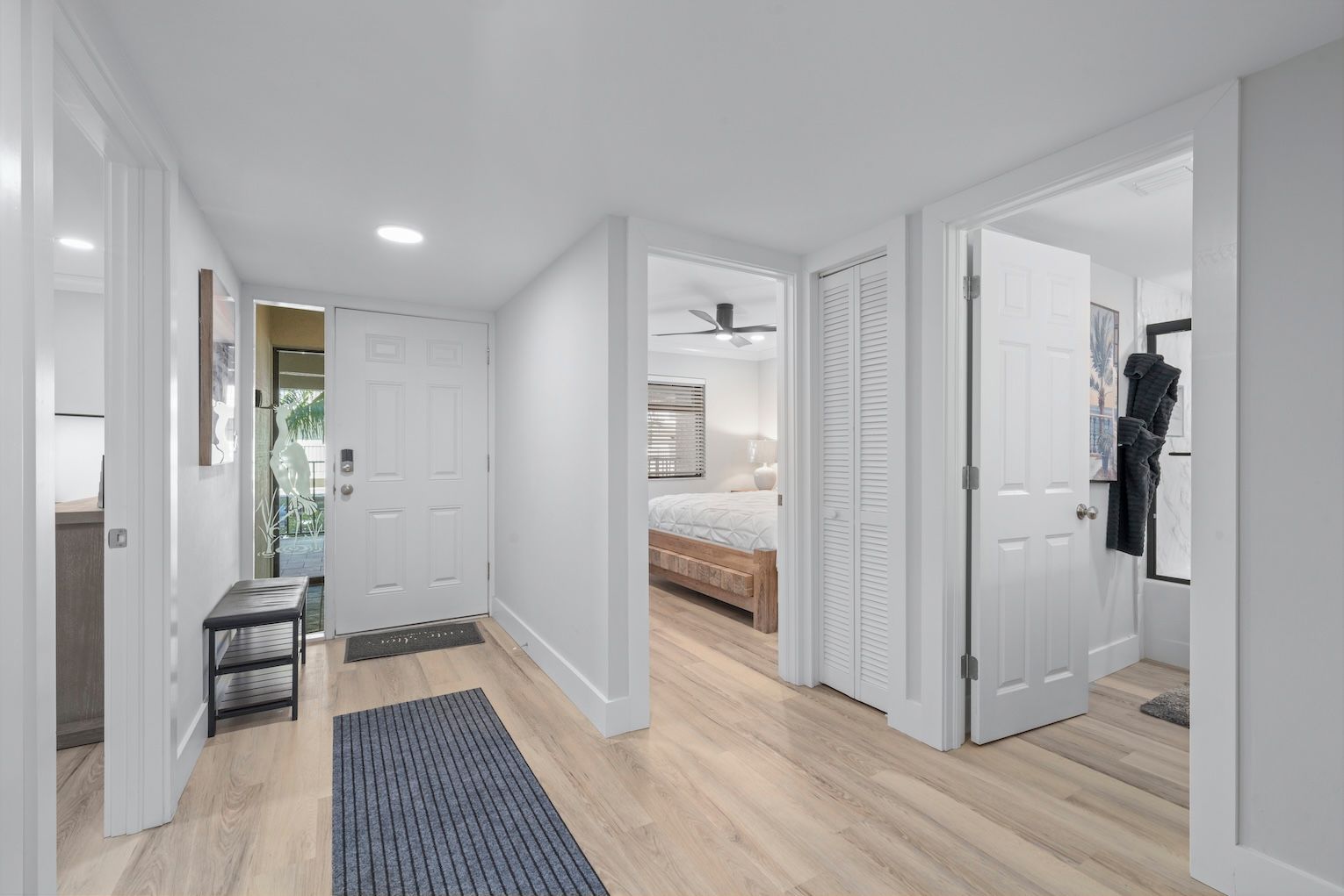 A hallway with a bench, a door leading to a bedroom, and a coat rack.
