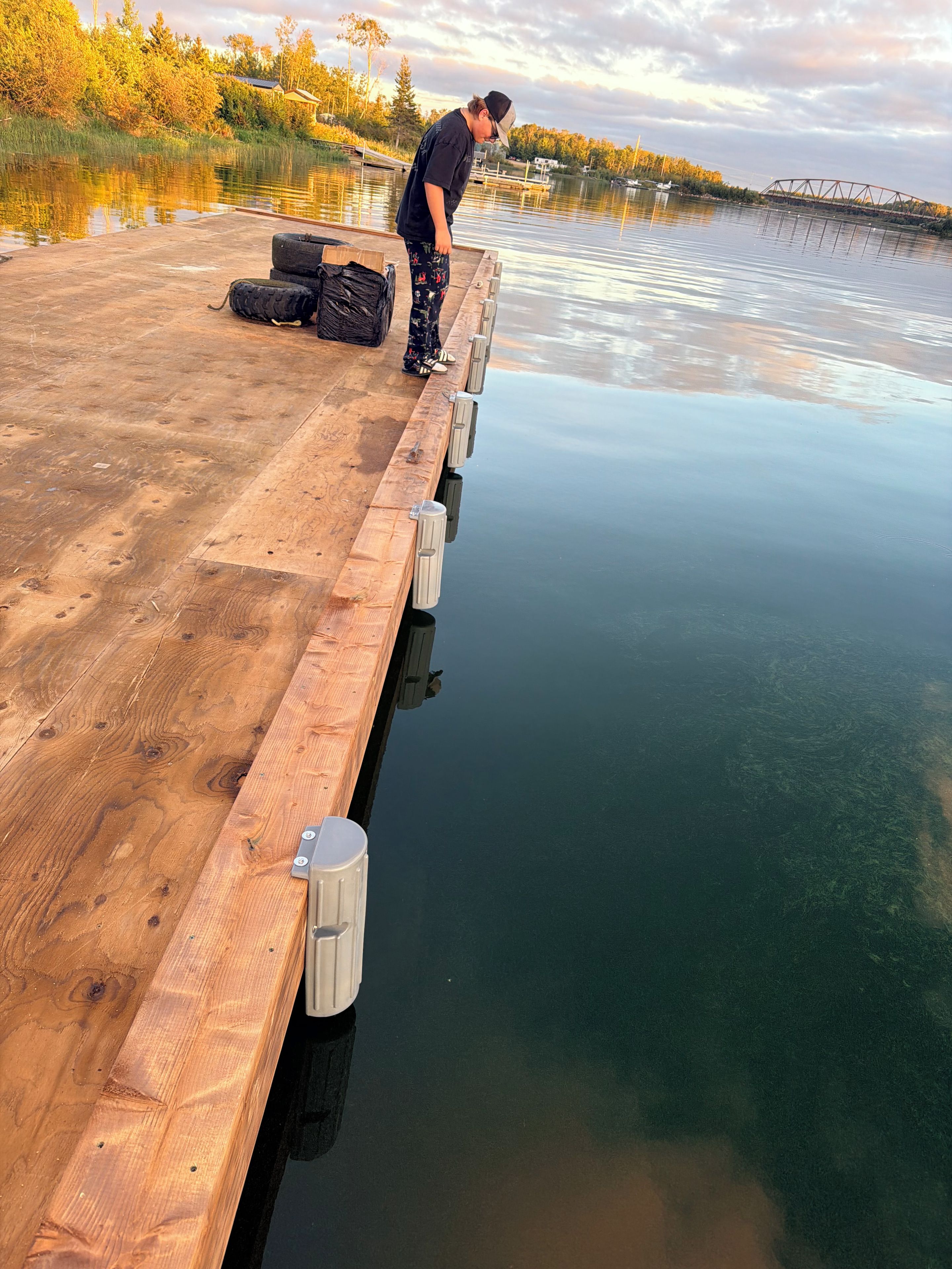 Une jetée en bois s’étendant dans une étendue d’eau calme, avec une personne debout à son extrémité.