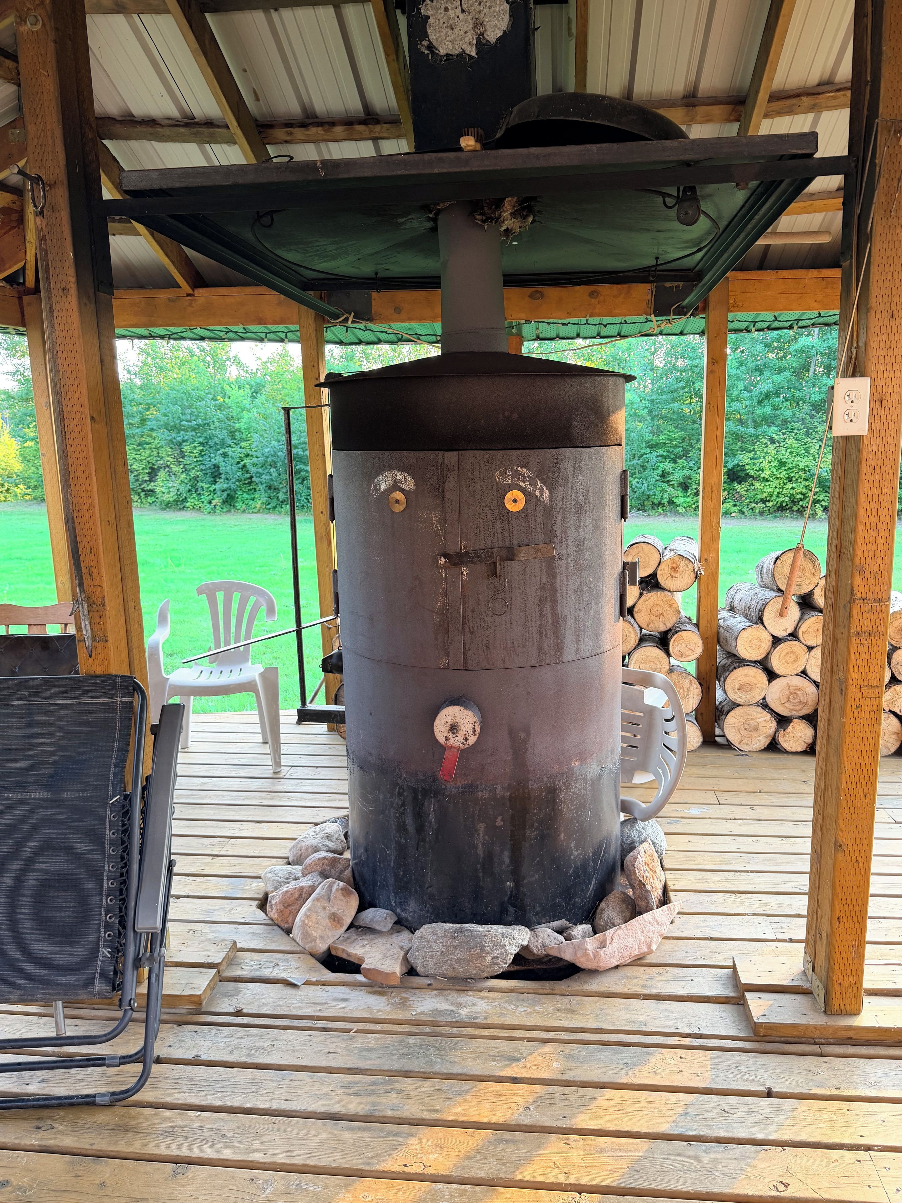 A rustic outdoor cooking area with a large stove, a chair, and a table.