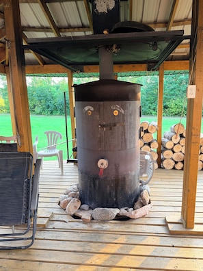 A rustic outdoor cooking area with a large stove, a chair, and a table.
