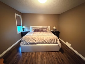 Une chambre à coucher avec un lit, des tables de chevet, une lampe et une fenêtre avec des stores.