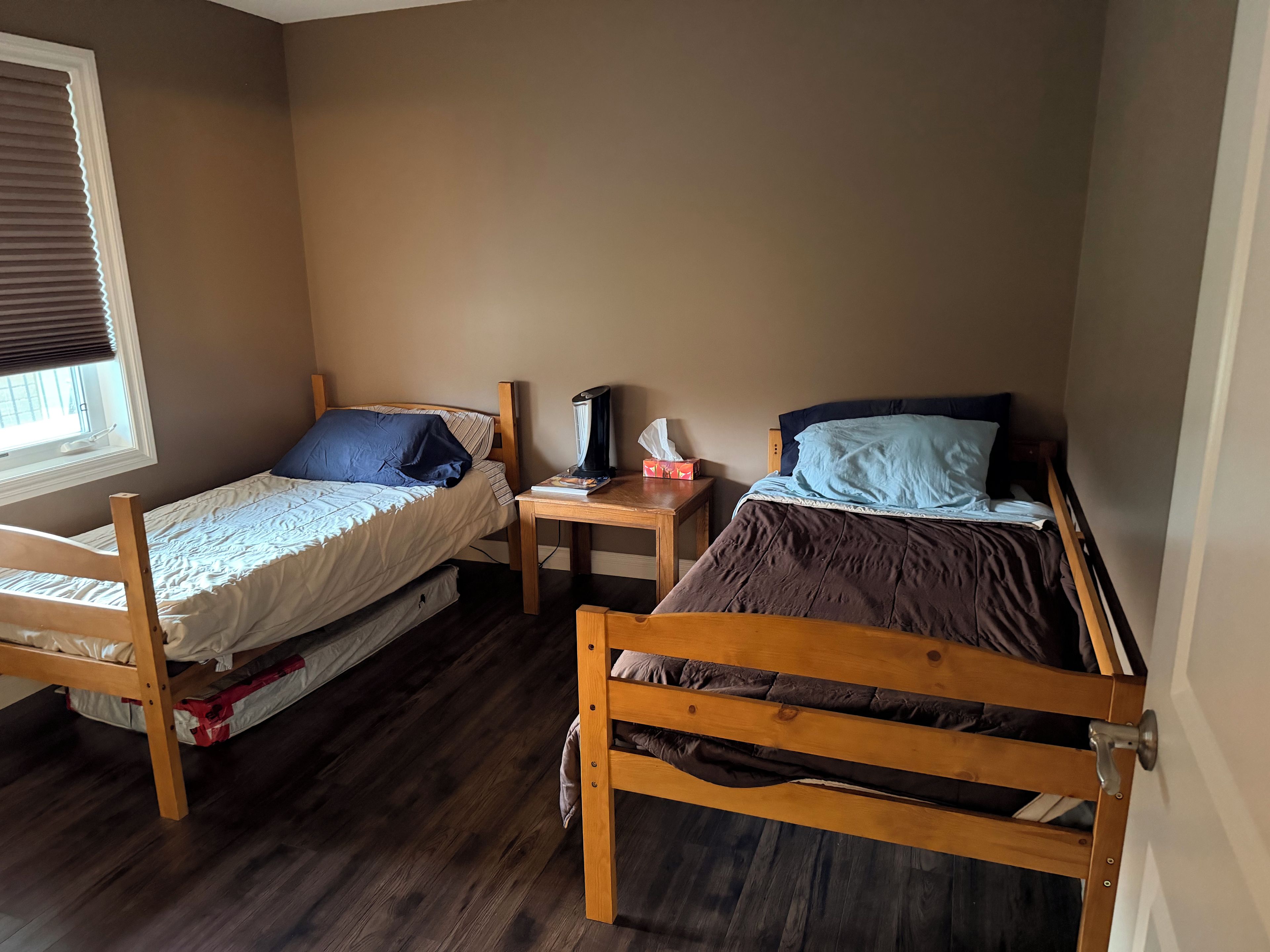 Une chambre avec deux lits superposés en bois, une table de chevet avec une lampe et une fenêtre avec des stores.
