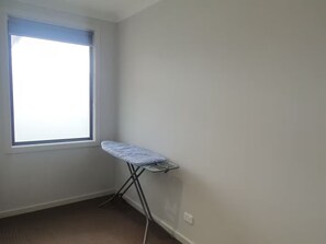 A room with a single window, a wall-mounted ironing board, and a carpeted floor.