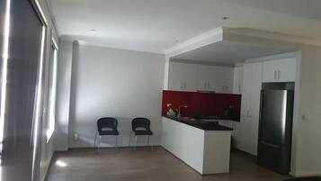 Una cocina moderna con armarios blancos, un salpicadero rojo y un refrigerador de acero inoxidable. En la zona de comedor contigua hay dos sillas y una mesa.