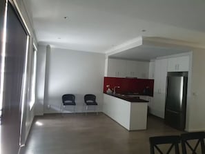 A modern kitchen with white cabinets, a red backsplash, and a stainless steel refrigerator. There are two chairs and a dining table in the adjacent dining area.