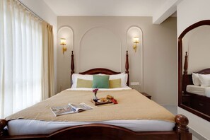A hotel room with a large bed, two wall-mounted lamps, a wooden headboard, and a mirror. - Elegant 2bhk w Pool Balcony in Candolim Pu-101 (Candolim)