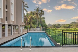 A swimming pool with a view of a lush green landscape and palm trees. - Elegant 2bhk w Pool Balcony in Candolim Pu-101 (Candolim)