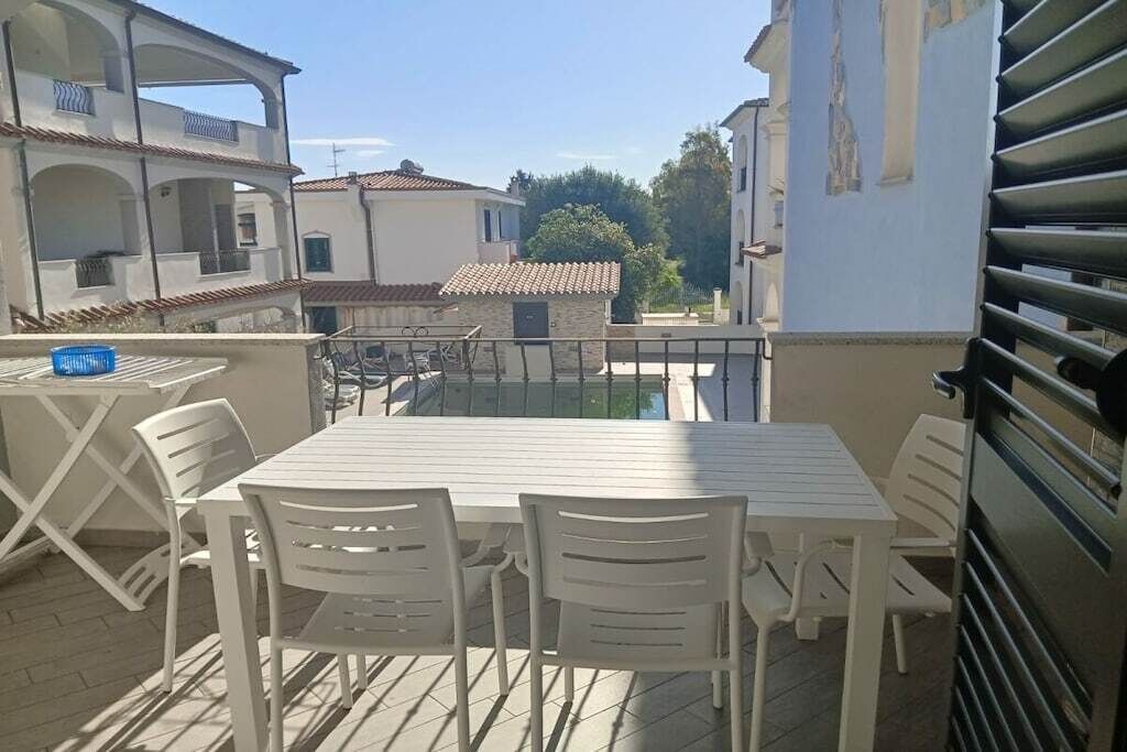 Un balcon avec une table et des chaises, donnant sur un quartier résidentiel avec des immeubles et un ciel dégagé.