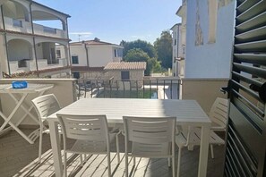 Een balkon met een tafel en stoelen, met uitzicht op een woongebied met gebouwen en een heldere lucht.