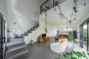 A modern living space with a staircase, a flat-screen TV, a sofa, and various potted plants. - Senja Villa – Peaceful modern villa in tropical Bali (Kediri)
