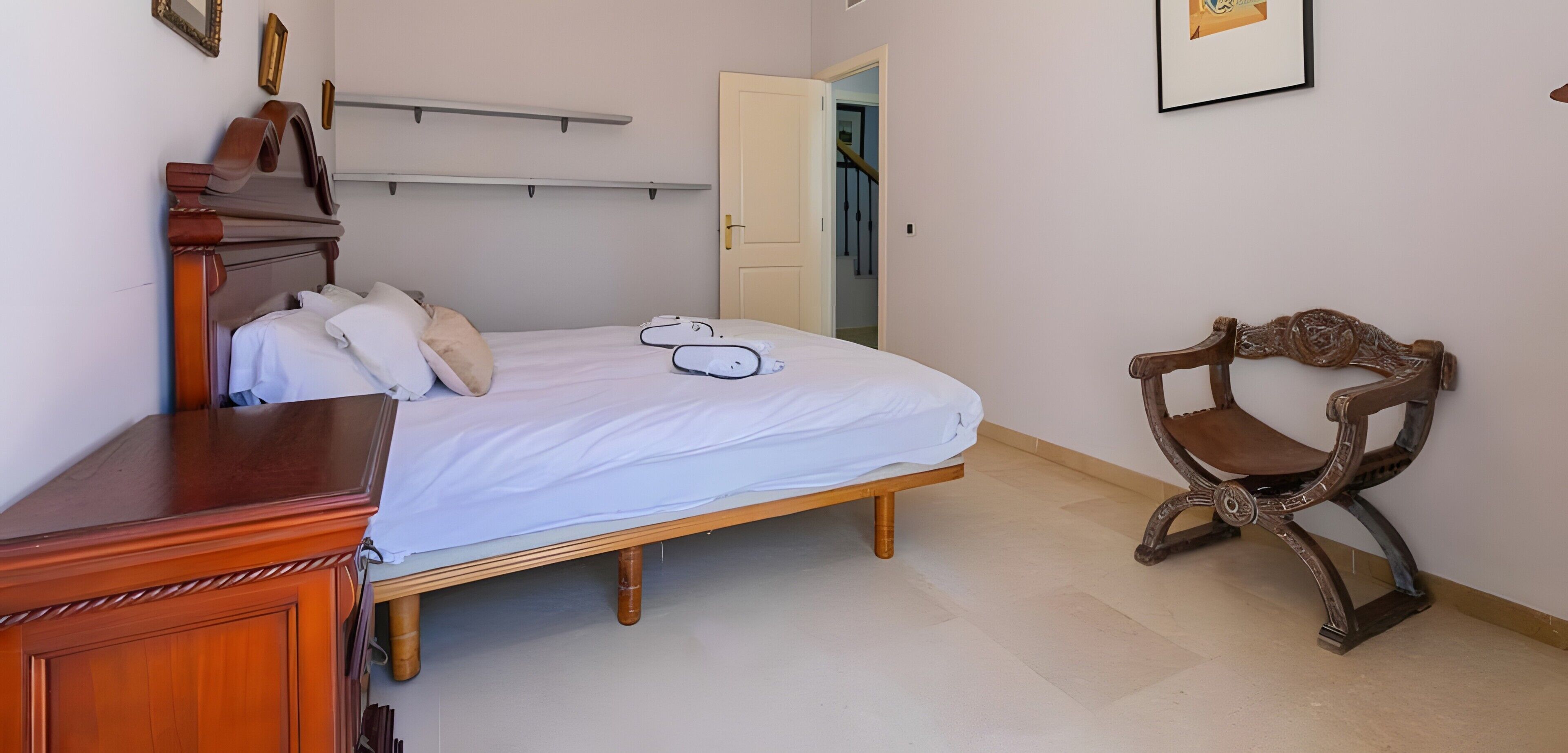 Ein Schlafzimmer mit einem hölzernen Bett, einem Sessel, einem Kleiderschrank und einer Tür zu einem anderen Raum.