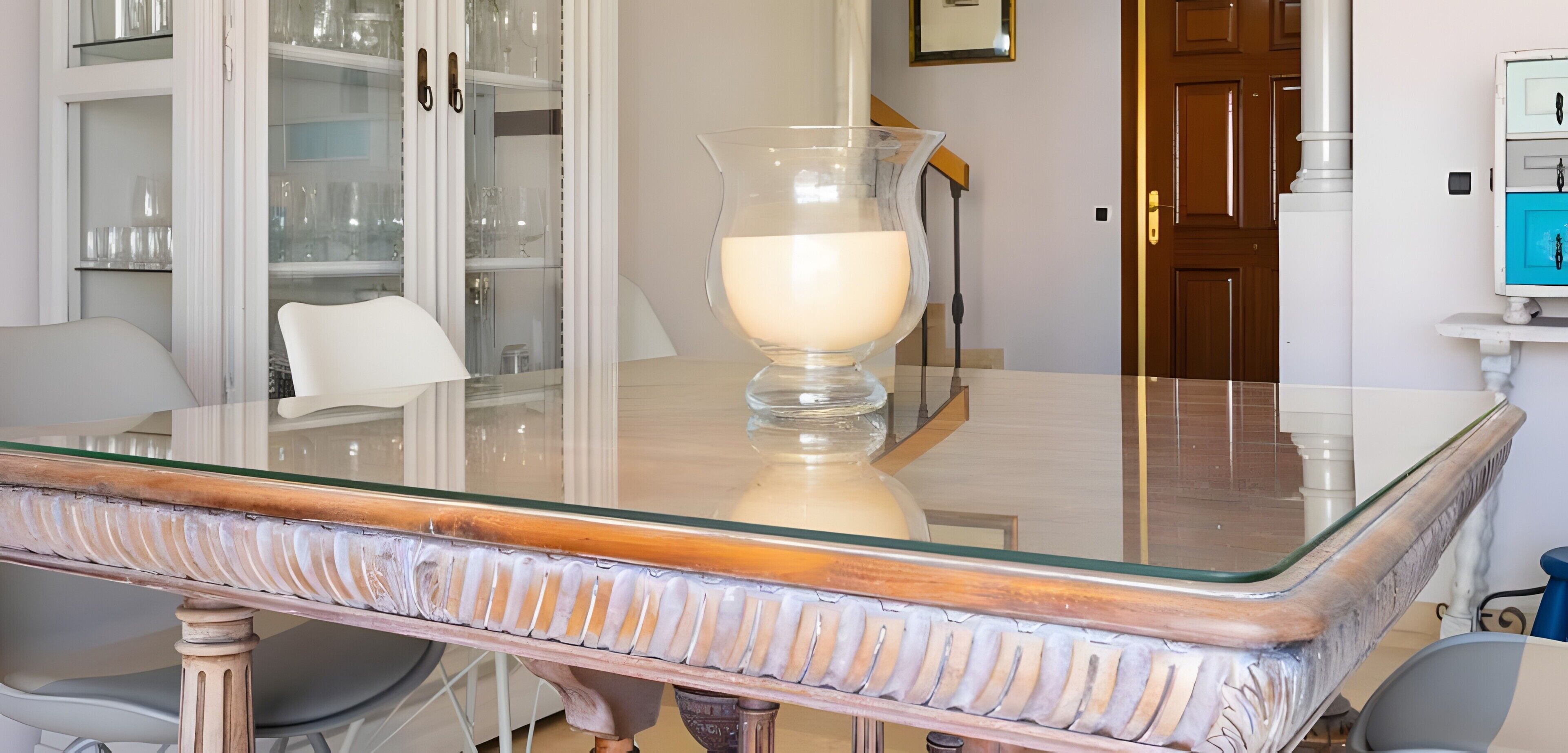 A dining table with a glass top and a white candle centerpiece.