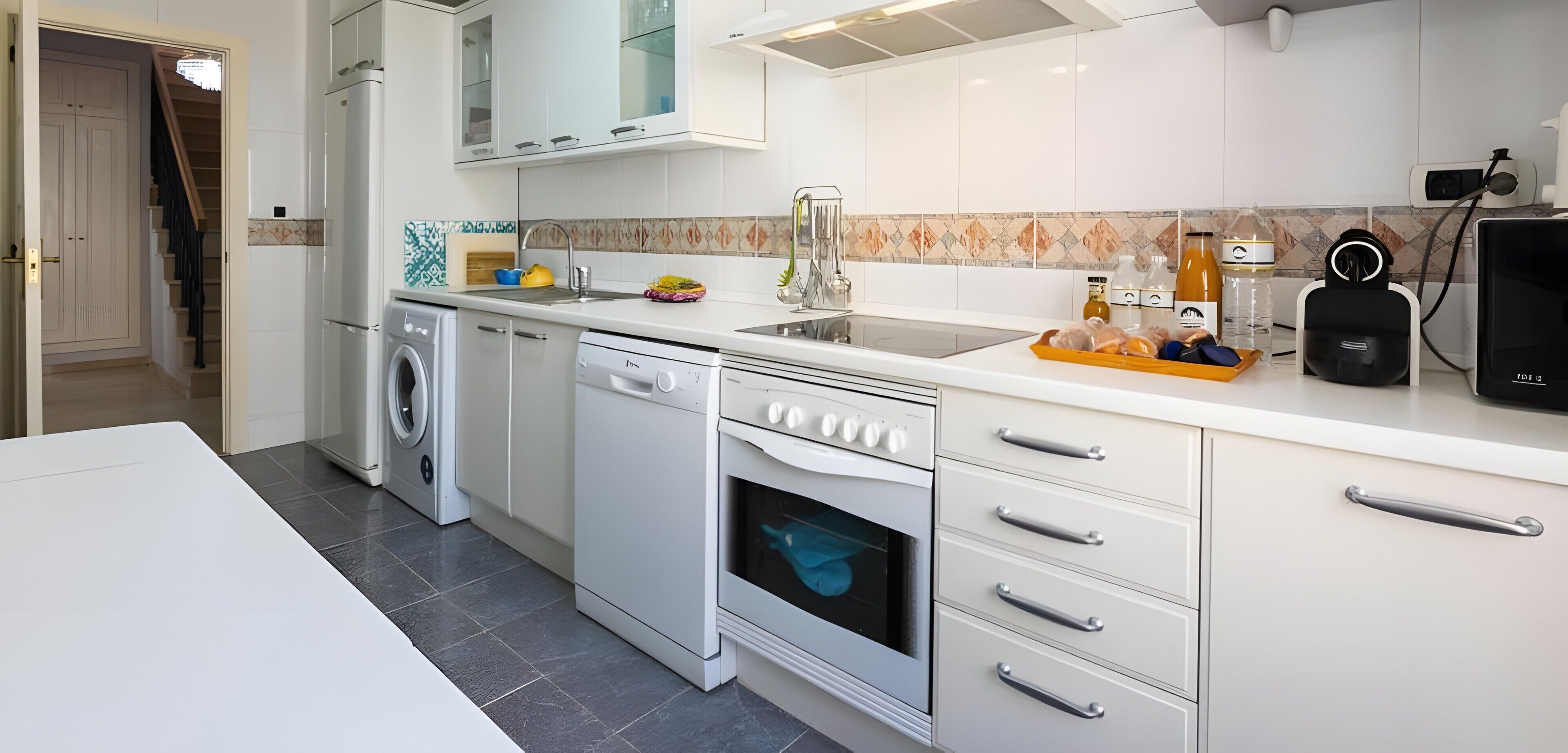 A modern kitchen with white cabinetry, a built-in oven, a dishwasher, and a countertop with various kitchen items.