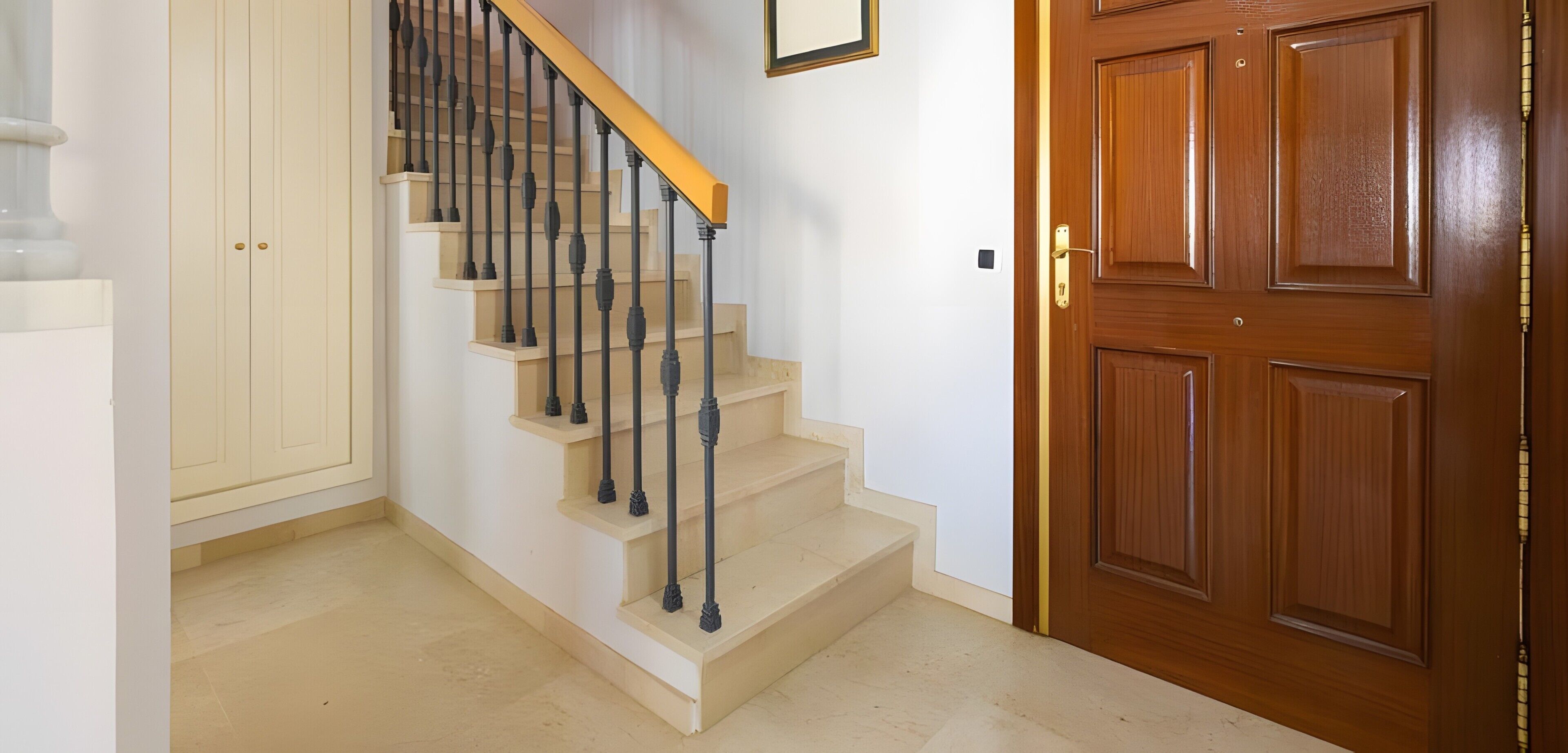 Eine Treppe mit einem Holzgeländer und schwarzen Spindeln, die zu einer Holztür mit Messinggriff führt.