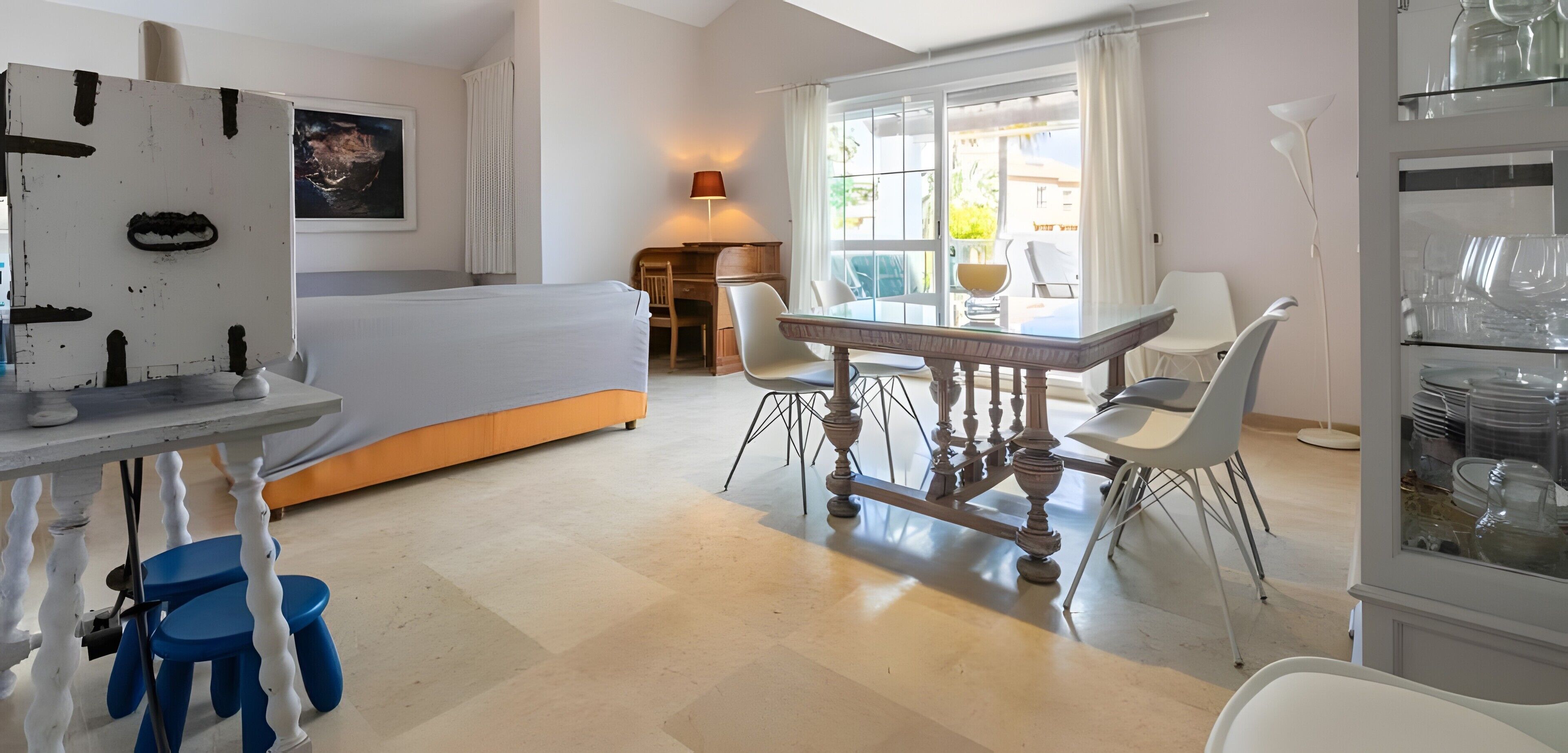 Une chambre à coucher avec un lit, un bureau et une chaise. Il y a une fenêtre avec des rideaux et une lampe sur le bureau.