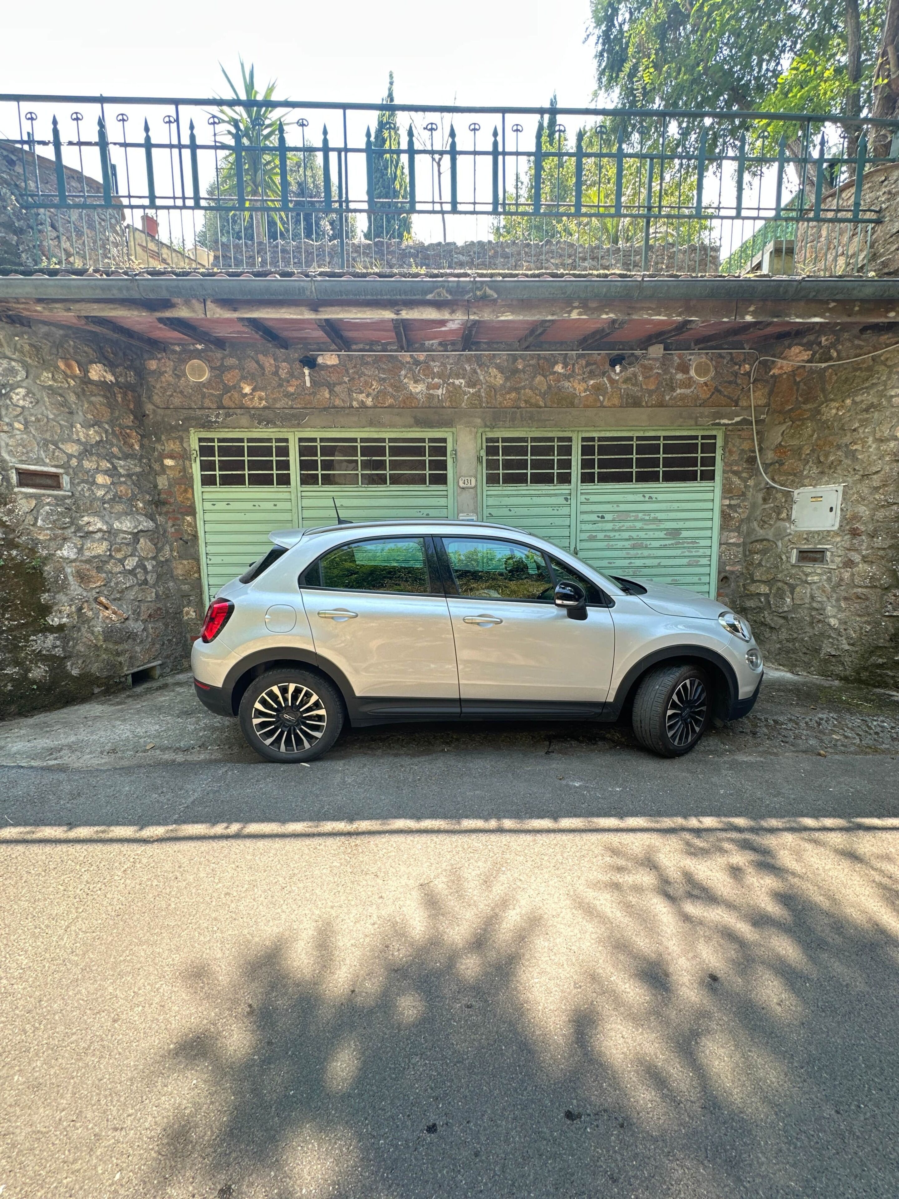 A silver car parked in front of a stone building with a green garage door.
