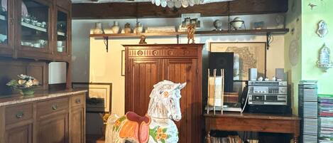 A rustic interior with exposed wooden beams, a rocking horse, a wooden cabinet, and a shelf with various items.