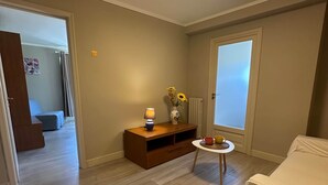 Een kamer met een witte bank, een klein tafeltje met een vaas en een lamp, en een houten kast.