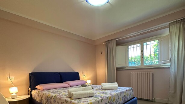 Een slaapkamer met een bed, nachtlampjes, een raam met gordijnen en een radiator.