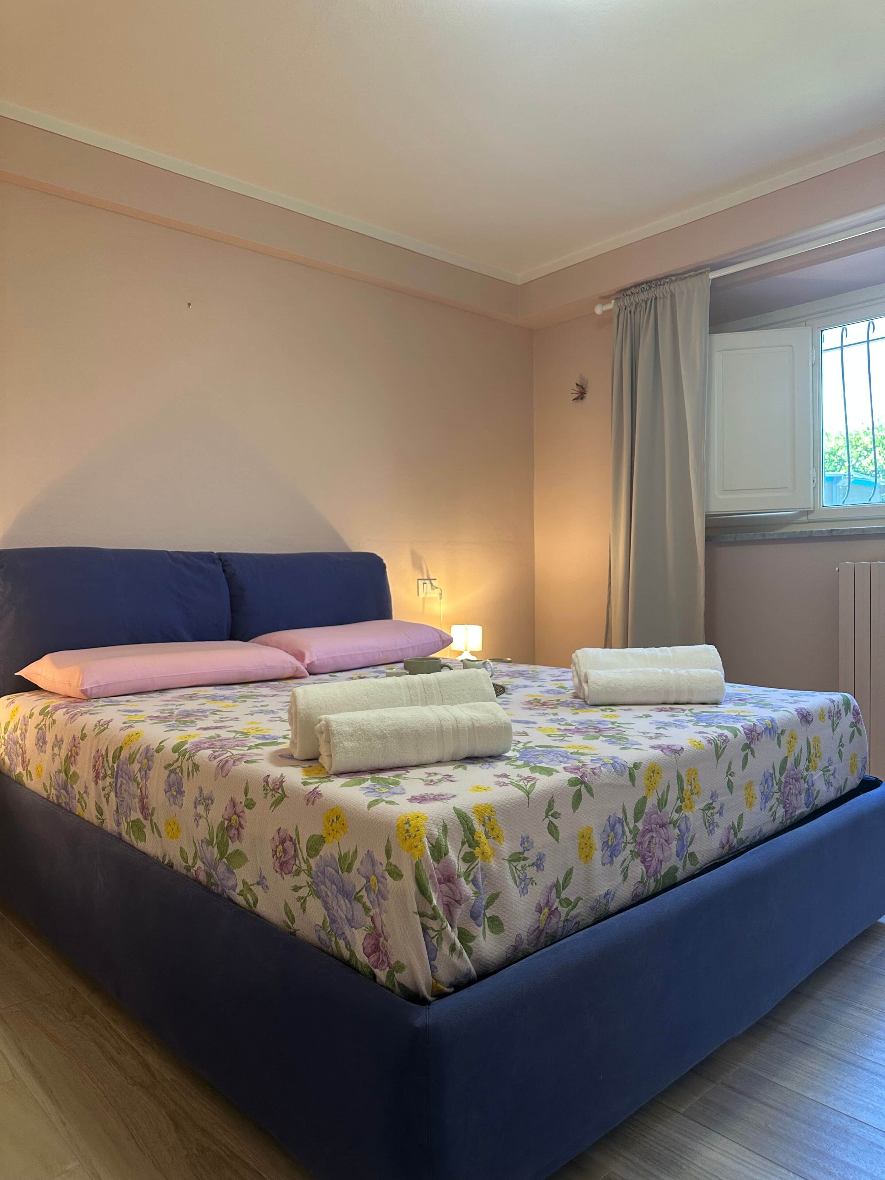 Ein Schlafzimmer mit einem Bett, Kissen, einer Nachttischlampe und einem Fenster mit Vorhängen.