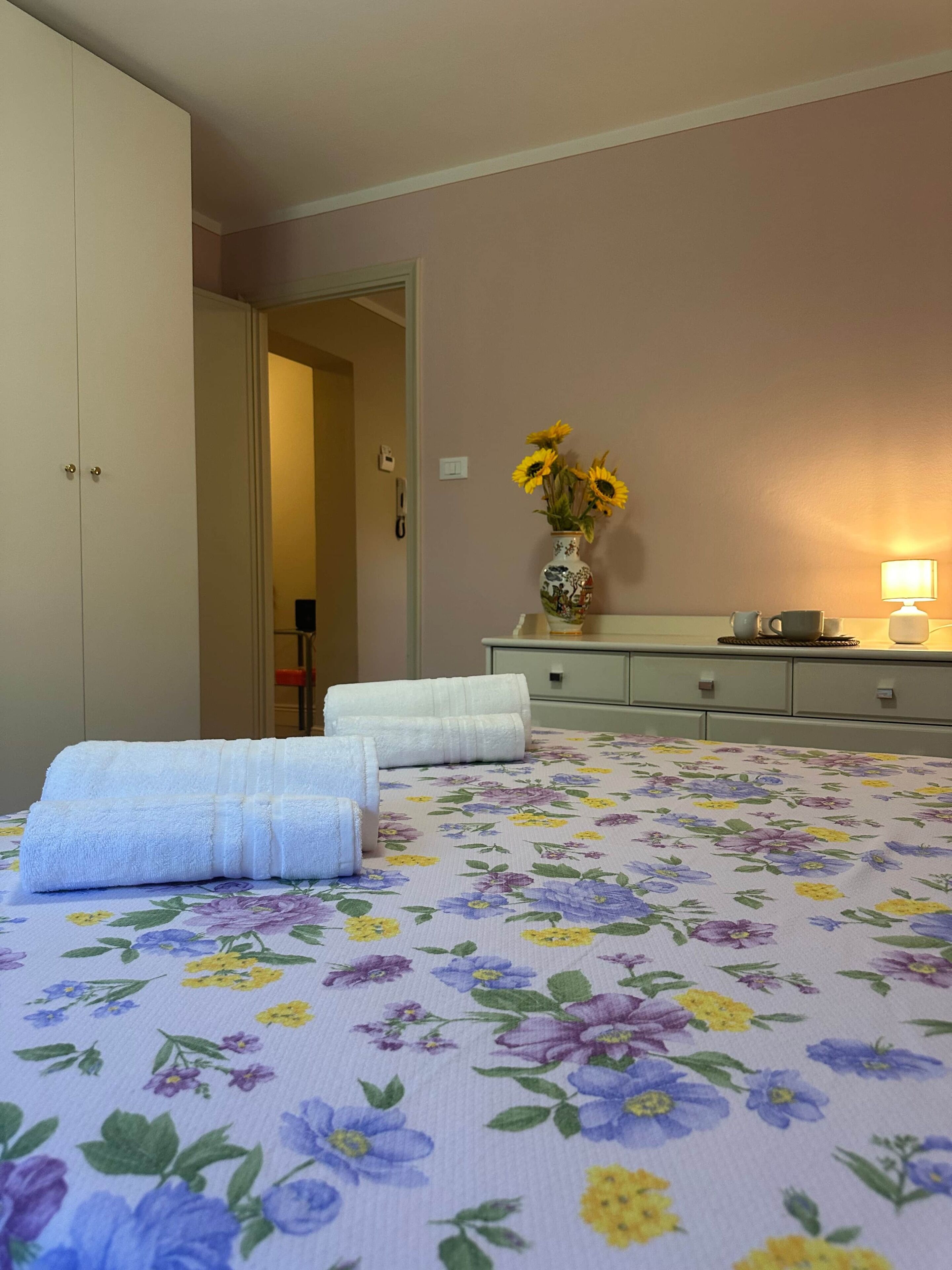 A hotel room with a bed, a nightstand, a lamp, and a vase with flowers.
