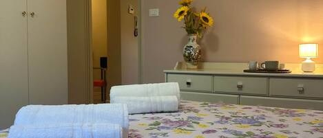 Ein Hotelzimmer mit einem Bett, einem Nachttisch, einer Lampe und einer Vase mit Blumen.