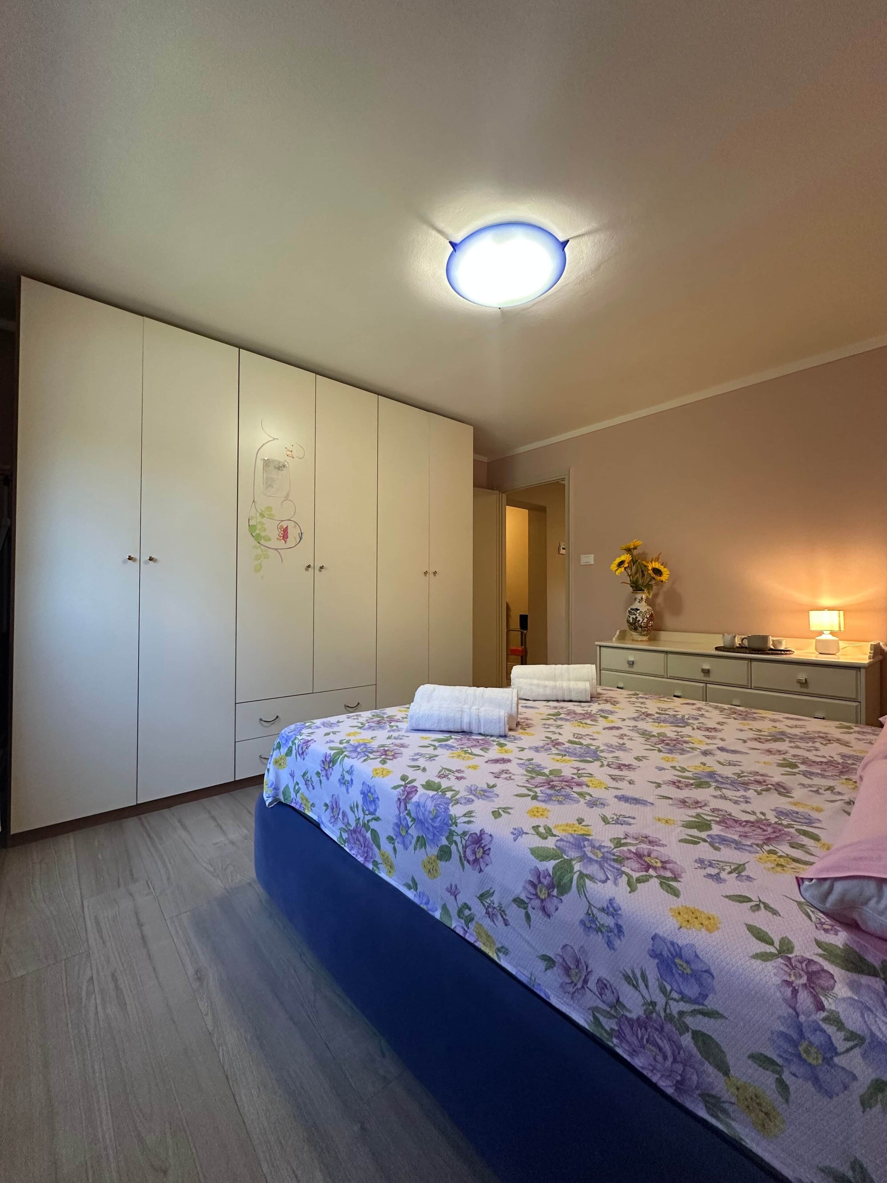 A bedroom with a bed, a wardrobe, a dresser, and a nightstand with a lamp.
