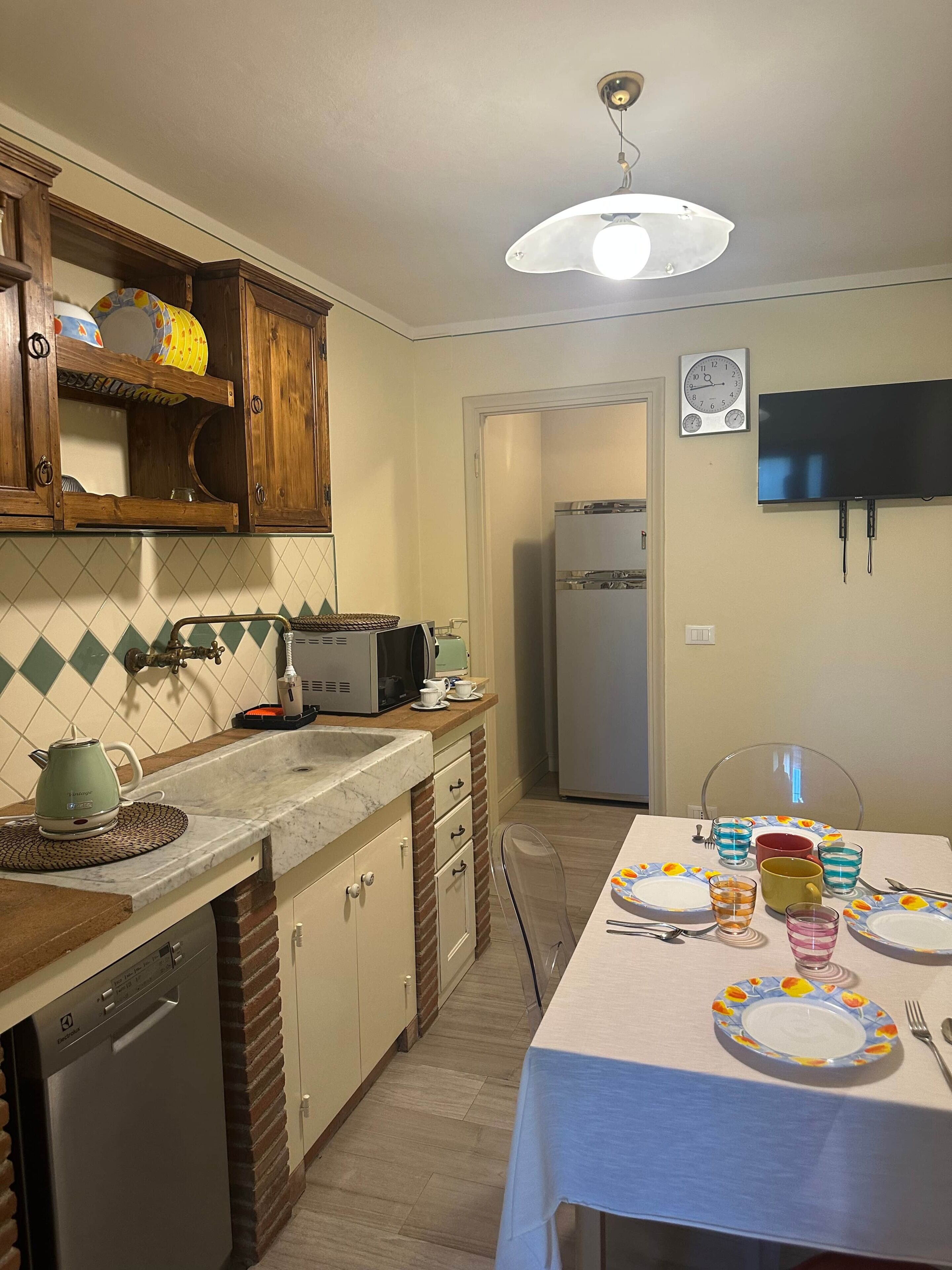 A kitchen with a dining table set for two, a microwave, a kettle, and a refrigerator.